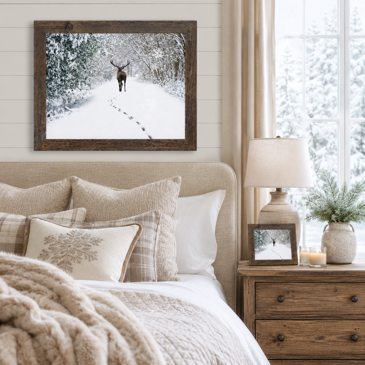 Natural brown framed winter stag wall art displayed above a beige tufted headboard in a cozy bedroom with layered knit, plaid, and embroidered snowflake pillows, a wood nightstand with a linen lamp and matching smaller piece, and snowy pine branches in a vase beside a window with falling snow visible outside