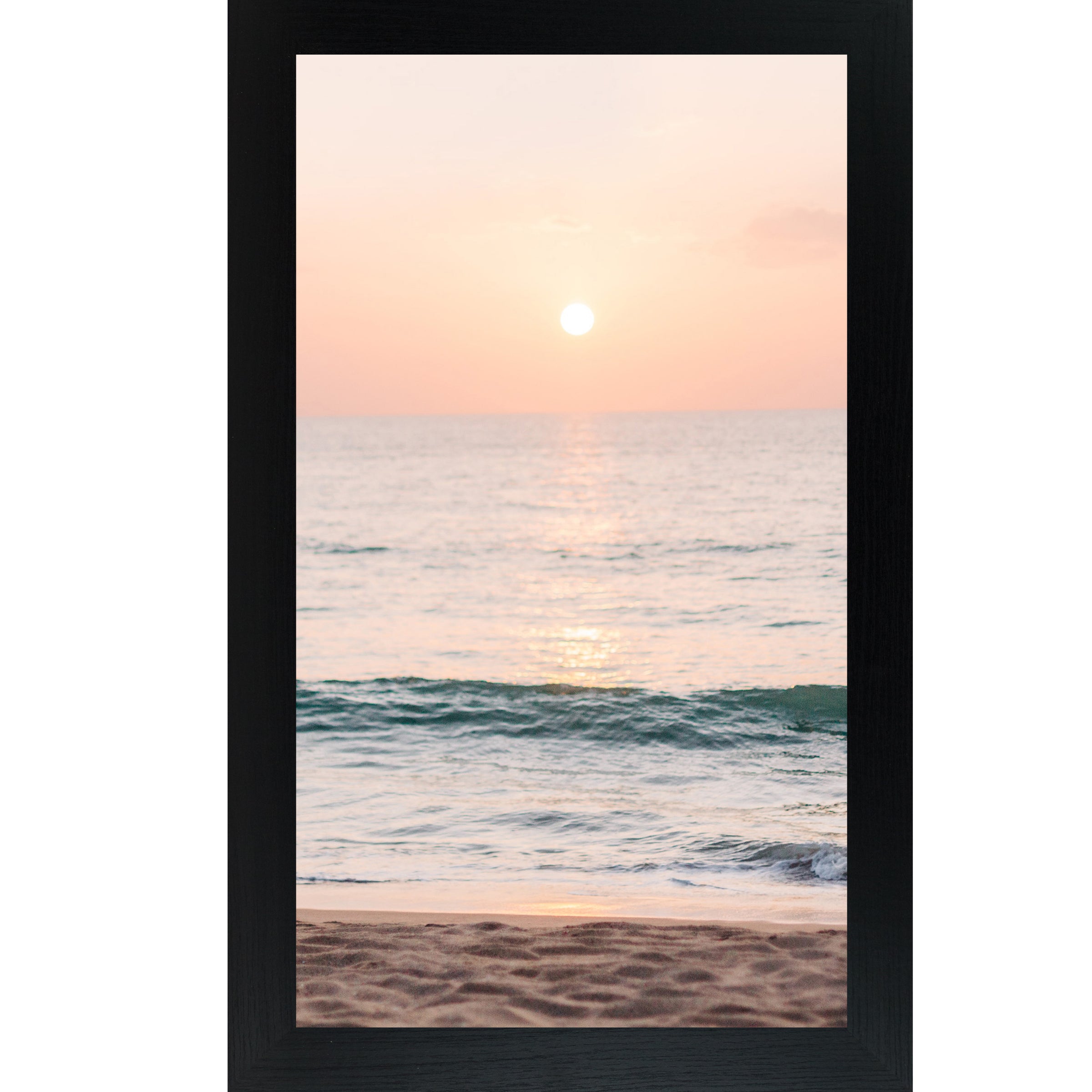 Black framed tall portrait beach sunset wall art featuring a glowing sun above the horizon with soft peach and coral sky, shimmering teal ocean waves, and sandy shoreline