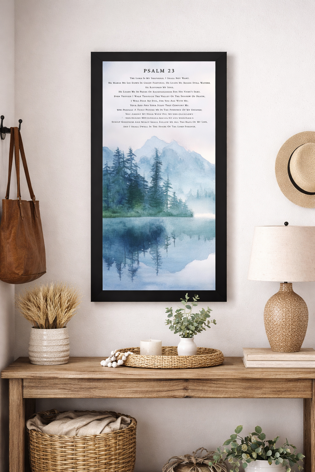 Black color Framed Psalm 23 wall art featuring a watercolor landscape of evergreen trees beside a mountain lake with blue reflections in the water. The scripture text appears above the misty mountain scene in a calm neutral design. Set in an entryway room