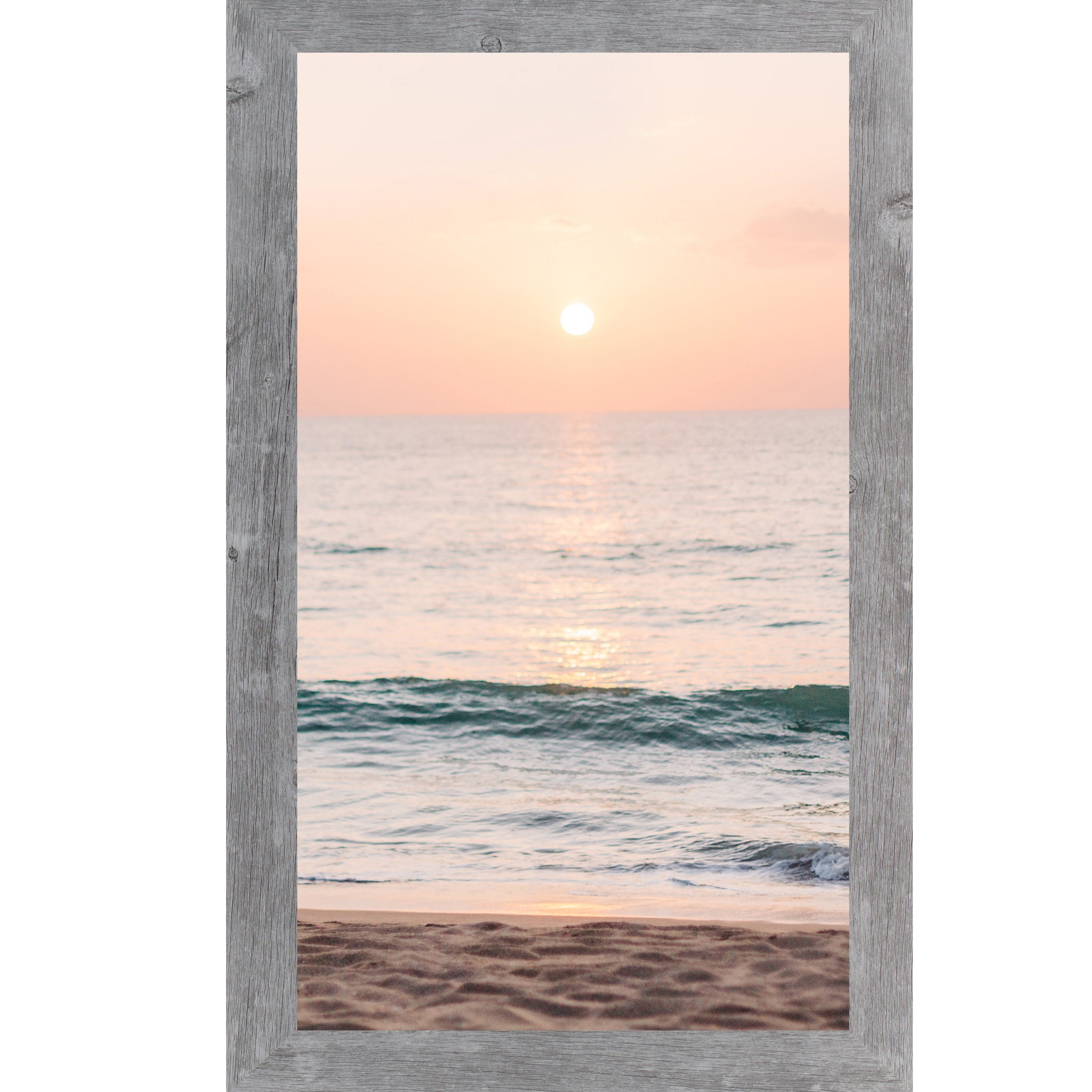 Gray framed tall portrait beach sunset wall art featuring a glowing sun above the horizon with soft peach and coral sky, shimmering teal ocean waves, and sandy shoreline