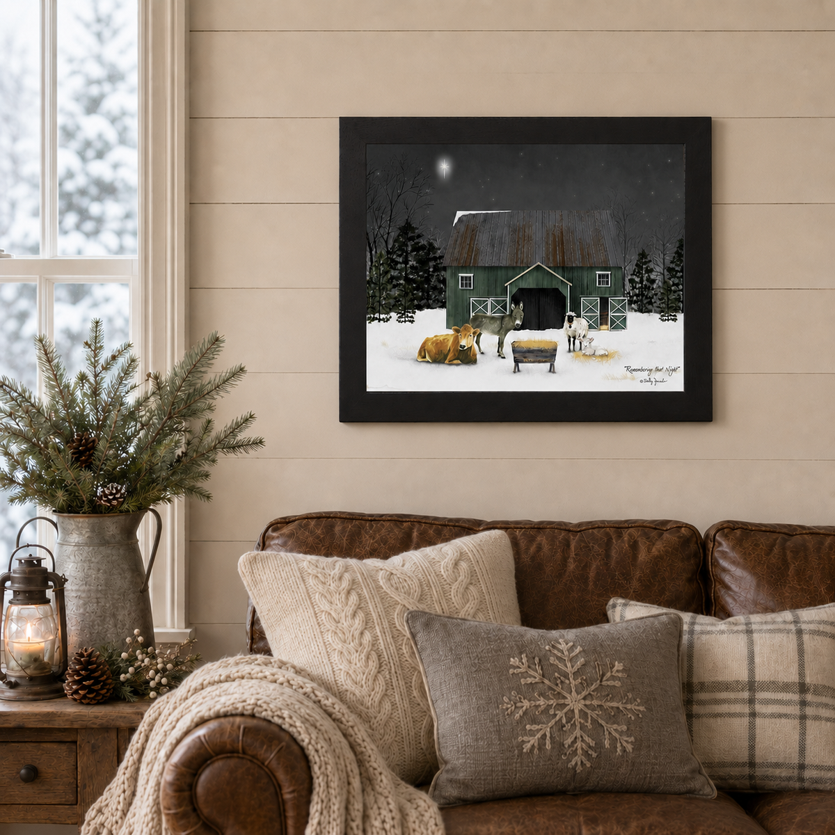 Black framed Billy Jacobs "Remembering That Night" landscape print displayed above a leather sofa in a cozy farmhouse living room with shiplap walls, pine branches in a galvanized pitcher, a lit lantern, and snowflake accent pillows