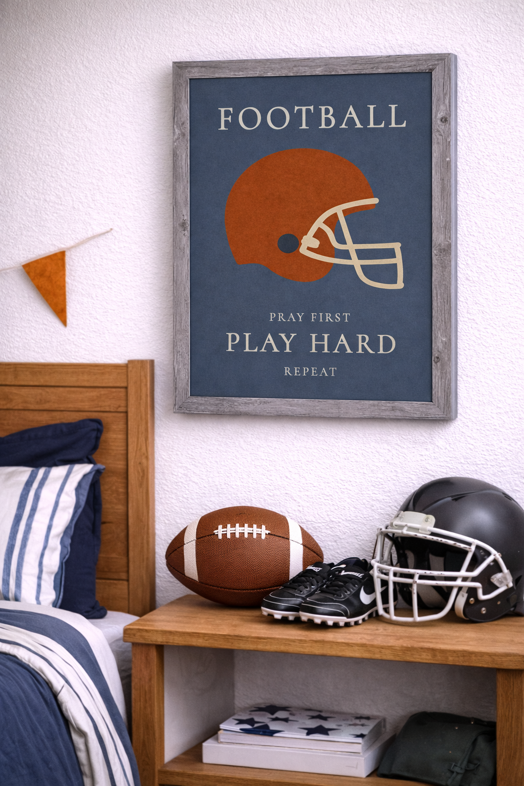 Room setting of a gray framed Christian football wall art featuring a football helmet with the phrase Pray First Play Hard Repeat on a blue background