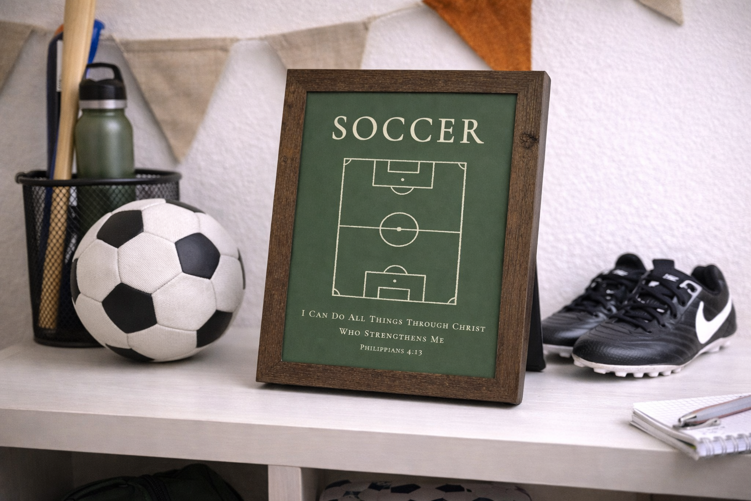Room setting showing a natural brown framed Christian soccer wall art featuring a soccer field diagram with the Bible verse Philippians 4:13 on a green background.