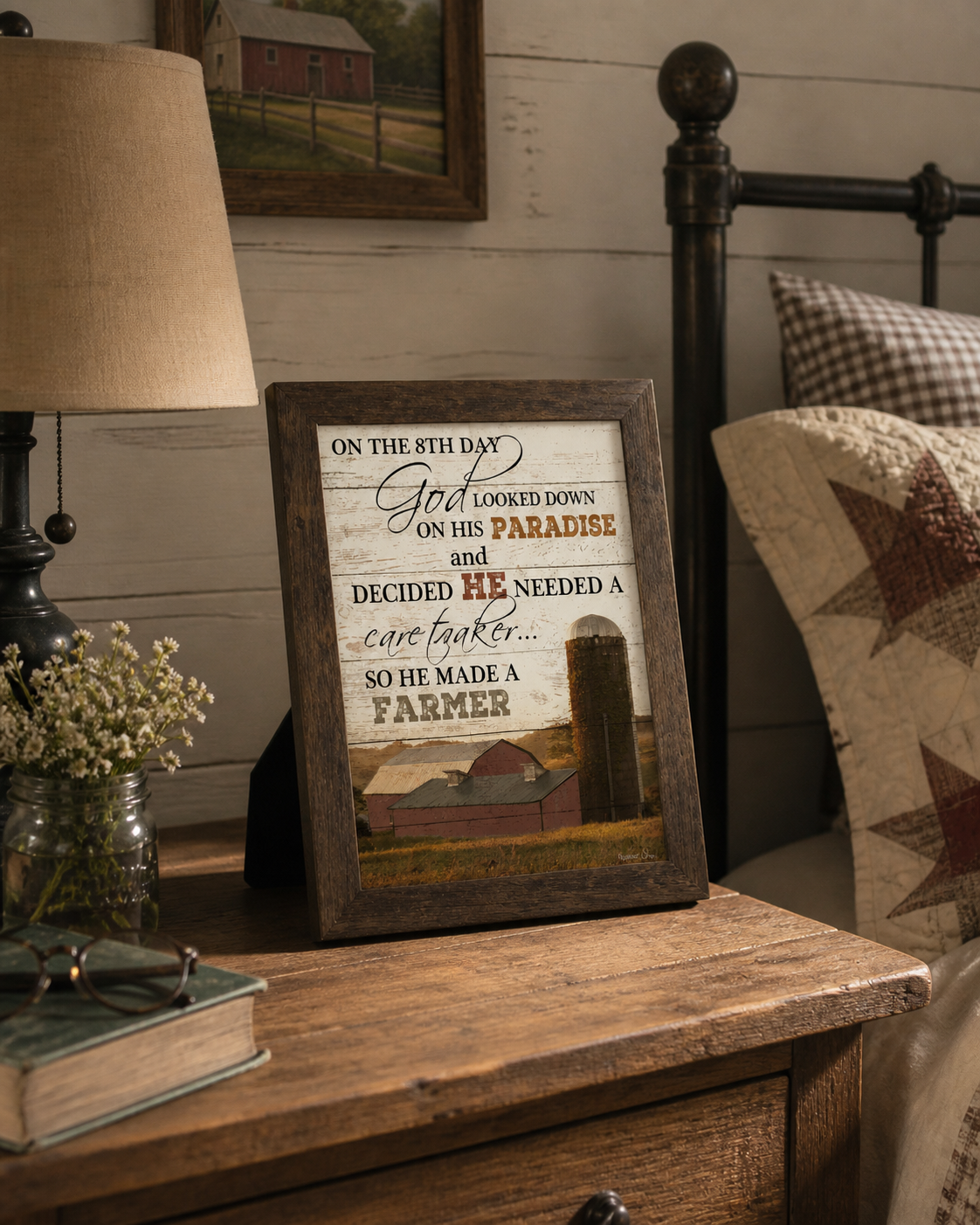 Natural Brown framed portrait farmhouse wall art with full On The 8th Day God Made A Farmer quote in bold mixed typography over red barn and ivy silo on rustic pallet wood background. In a bed room setting on a nightstand.