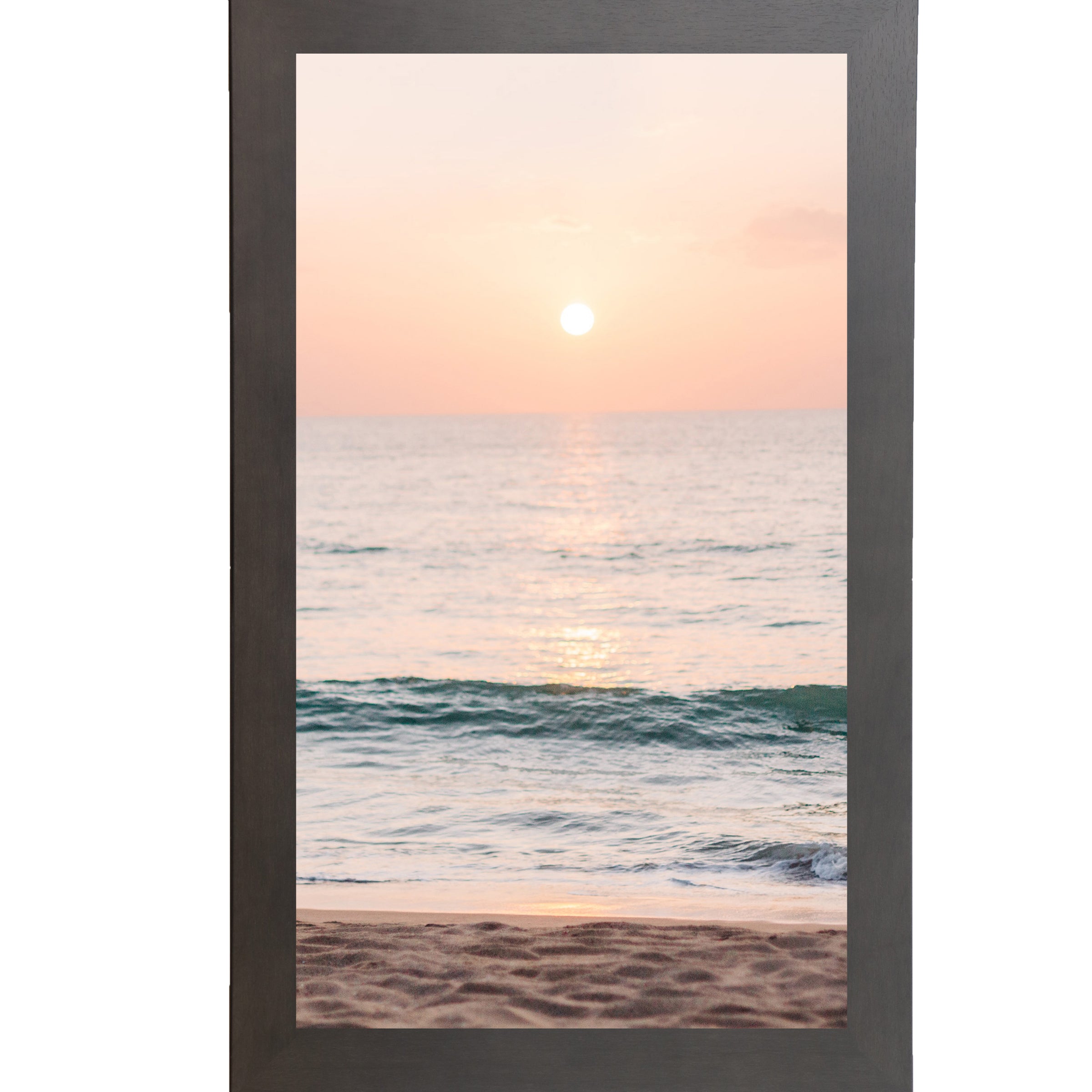 Slatewood framed tall portrait beach sunset wall art featuring a glowing sun above the horizon with soft peach and coral sky, shimmering teal ocean waves, and sandy shoreline